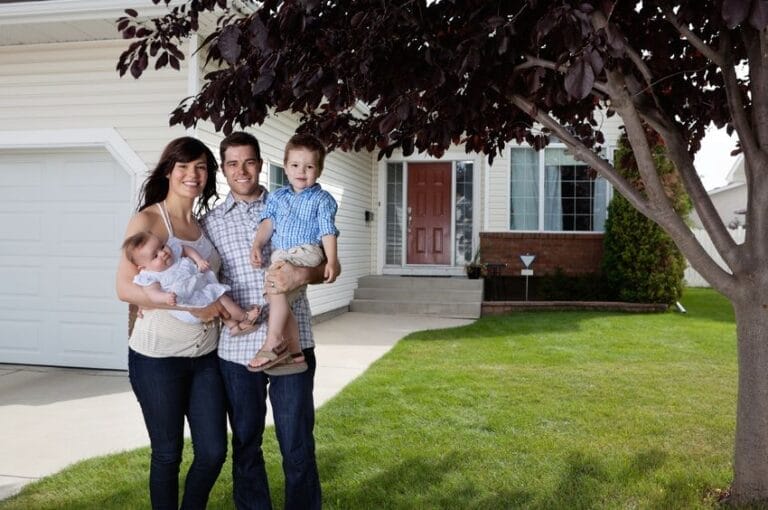 Young couple with 2 kids on the front lawn in front of their home