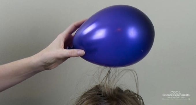 Static electricity demonstration by holding a balloon over a person's head to see hair raising up. 