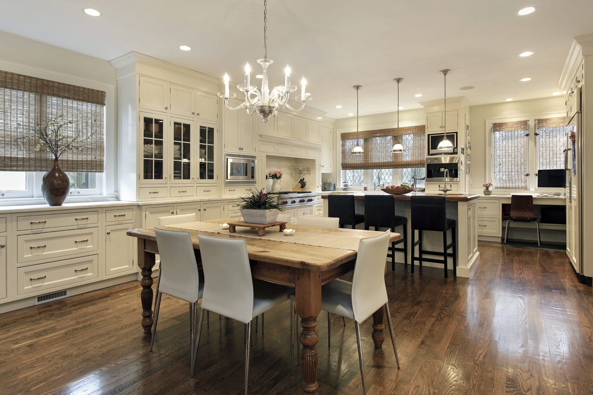 Spacious kitchen with white cabinetry, a wooden dining table and chairs, a chandelier, hardwood floors, and ample natural light from large windows with woven shades. The premium electric appliances make cooking a breeze in this bright and welcoming space.