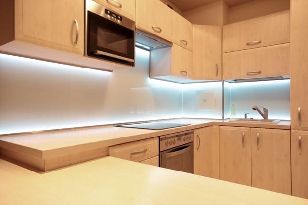 A newly renovated kitchen with light wooden cabinets and under cabinet lighting.