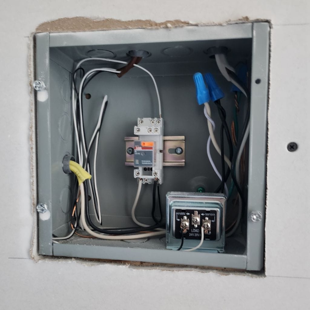 An electrical junction box with various wires connected to terminals, including a relay and a current sensor, is securely housed inside a cut-out wall section, showcasing the quality of Premium Electric components.