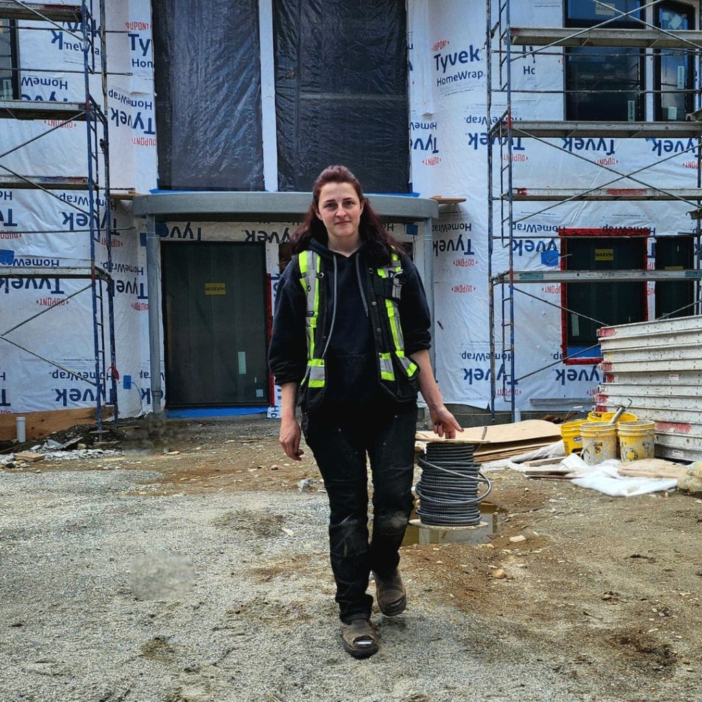 Person in construction attire carrying coiled wire, standing on a construction site with a partially constructed building and scaffolding in the background, representing Premium Electric's commitment to quality and excellence.