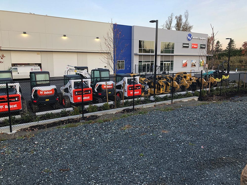 An outdoor lot with various construction machinery, including Bobcat vehicles, parked behind a chain-link fence. A commercial building with a "Western Equipment" sign in the background showcases their Premium Electric services and equipment.