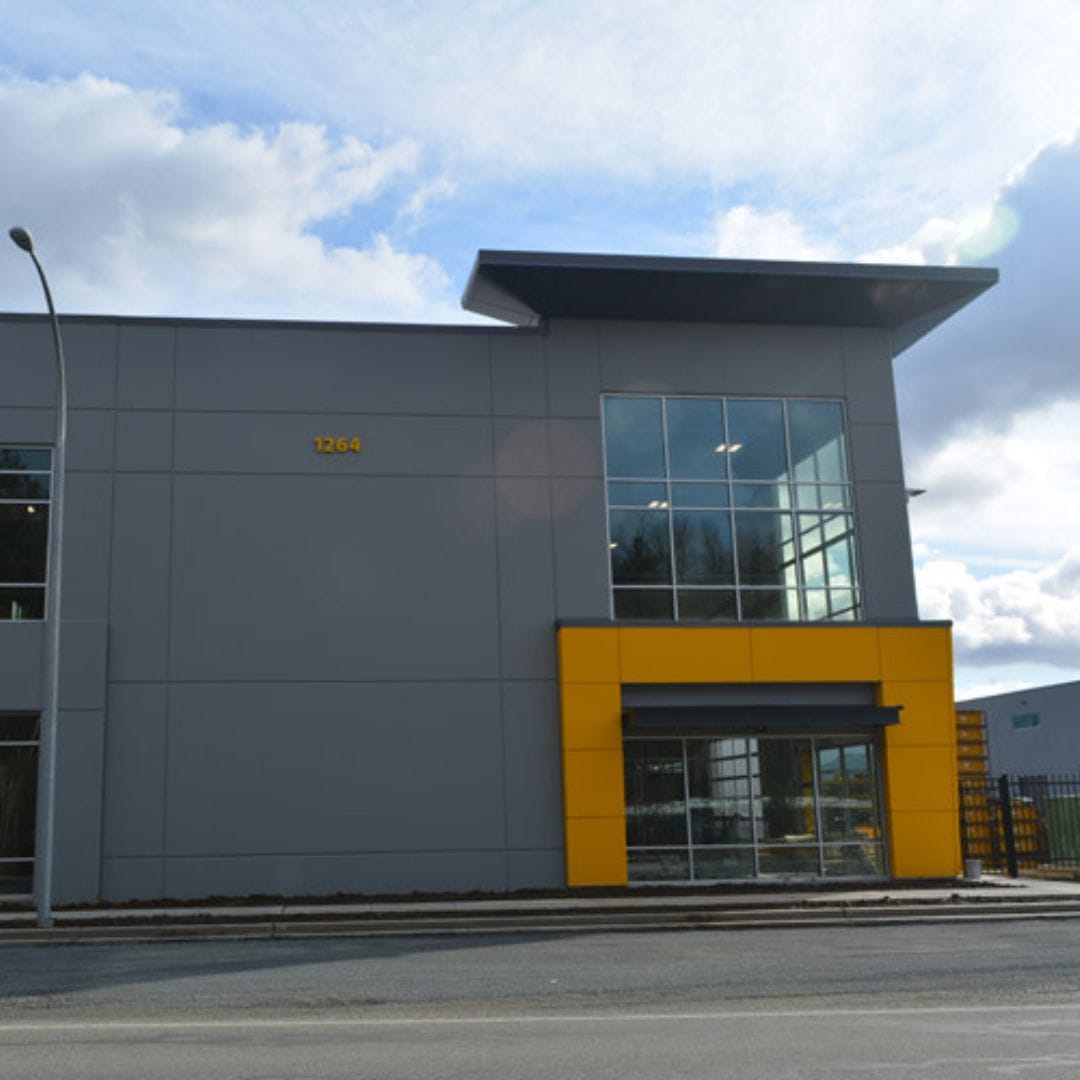 A modern commercial building with a yellow accent section, large glass windows, and the number 1264 displayed on the exterior. The sky is partly cloudy, creating the perfect backdrop for Premium Electric's sleek new headquarters.