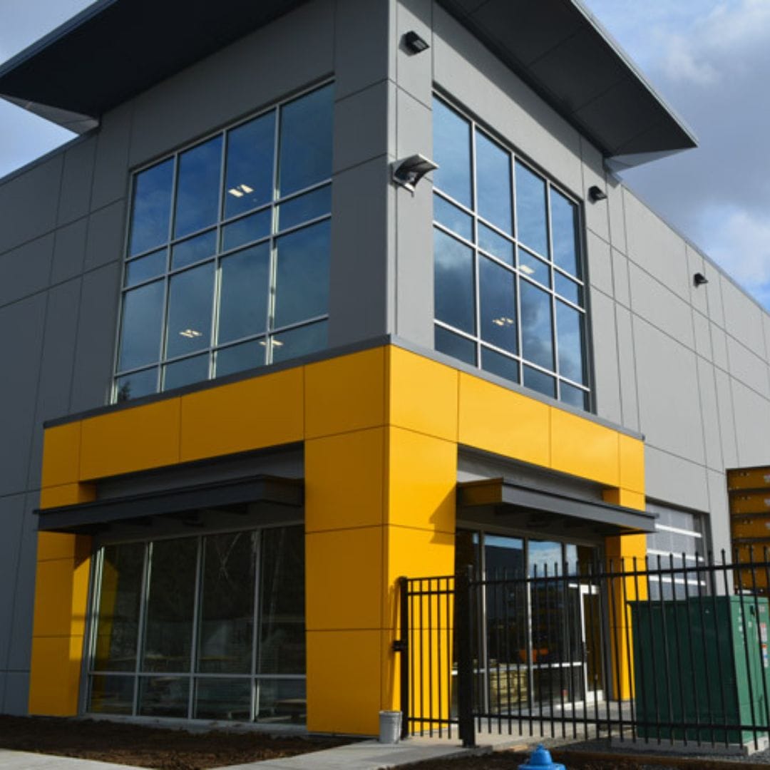 A modern two-story commercial building with large windows and a vibrant yellow entrance, equipped with Premium Electric solutions throughout.