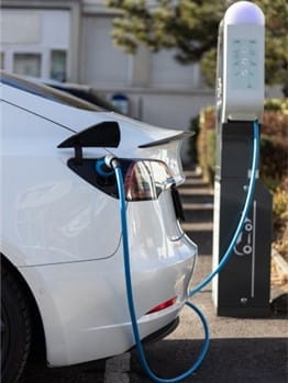 Electric car charging at a charging station with a blue cable in a parking area.